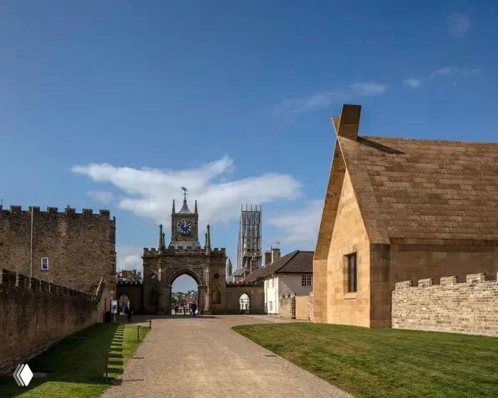 Наружный вид колледжа в Кембридже: арка, исторические и современные каменные корпуса на фоне ясного неба и аккуратного газона.