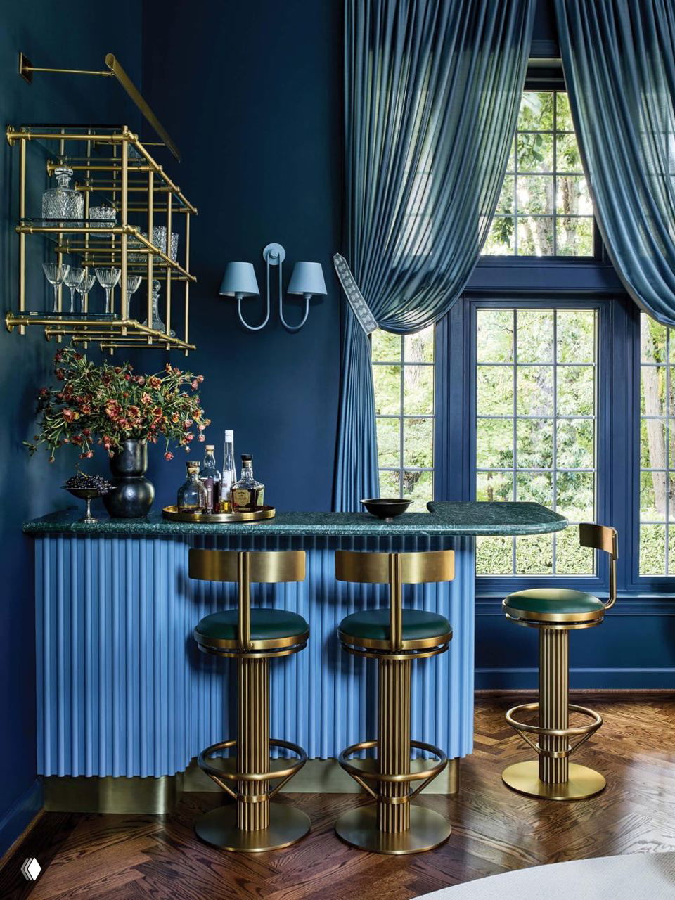 Барная зона в насыщенных синих тонах: рифленый бар с мраморной стойкой, позолоченные барные стулья и большие окна с драпировками, создающие камерную атмосферу.
