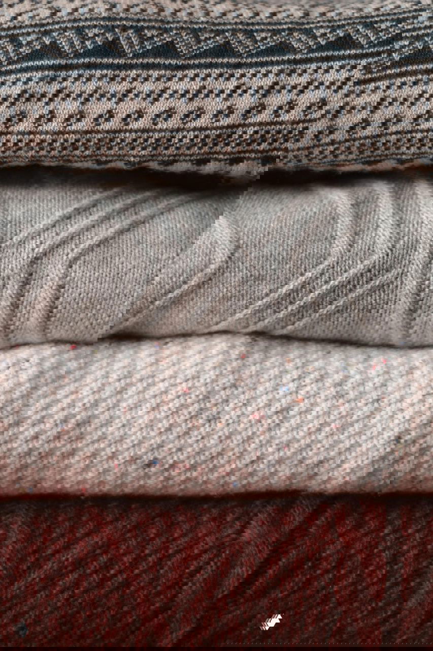 Крупный план аккуратно сложенных свитеров разной фактуры и цвета, иллюстрирующий метод Конмари и правила компактного вертикального складывания одежды.