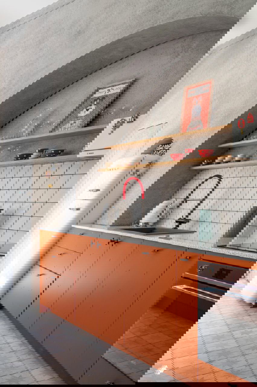 Кухонный гарнитур с матовыми оранжевыми фасадами в сочетании с серыми стенами и декоративной аркой, рабочая зона оформлена в мягких нейтральных тонах