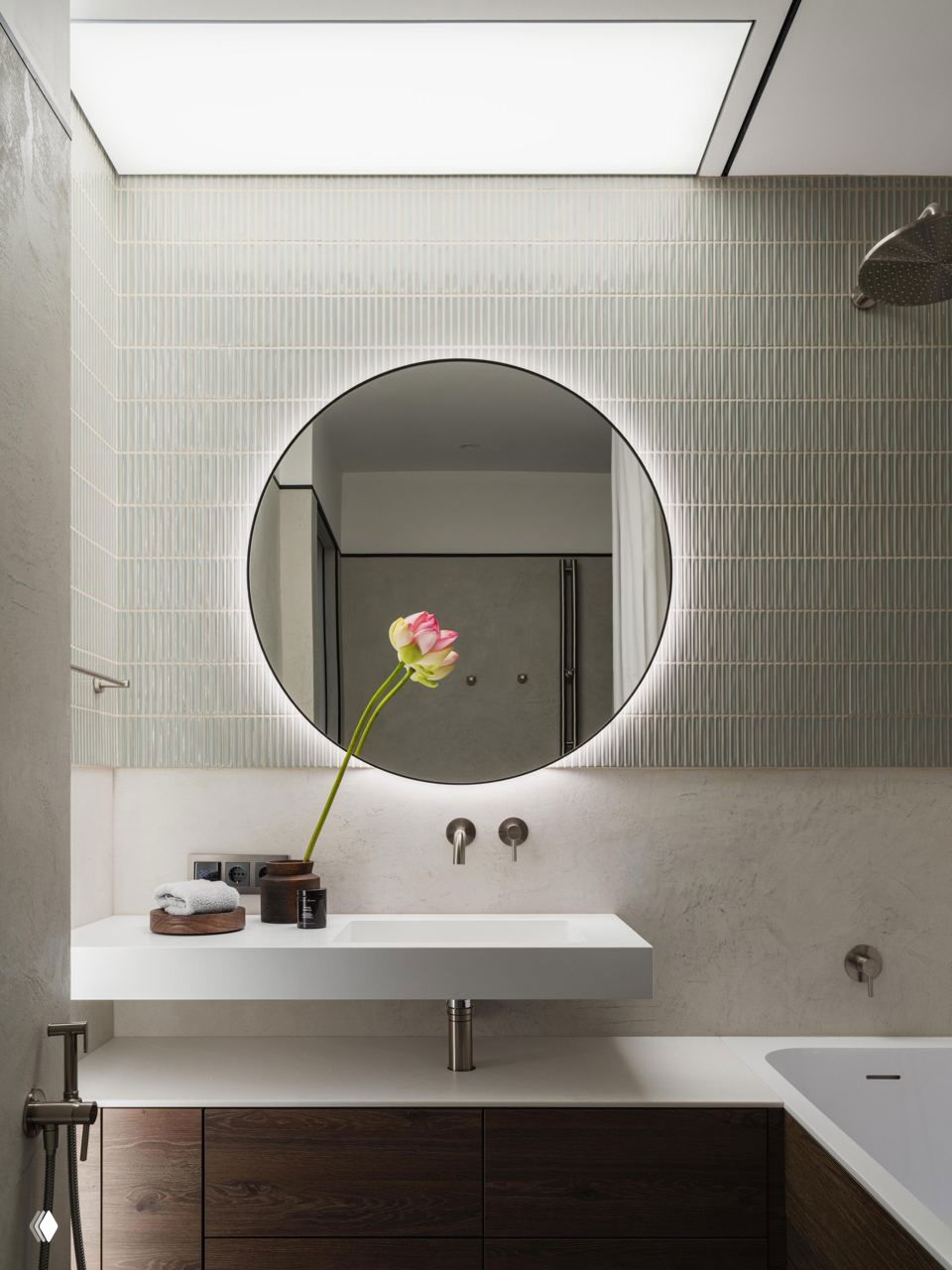 Ванная комната с круглым подсвеченным зеркалом, узкой вертикальной плиткой и белой выдвижной раковиной на фоне дерева и светлого камня — минималистичный свежий интерьер.