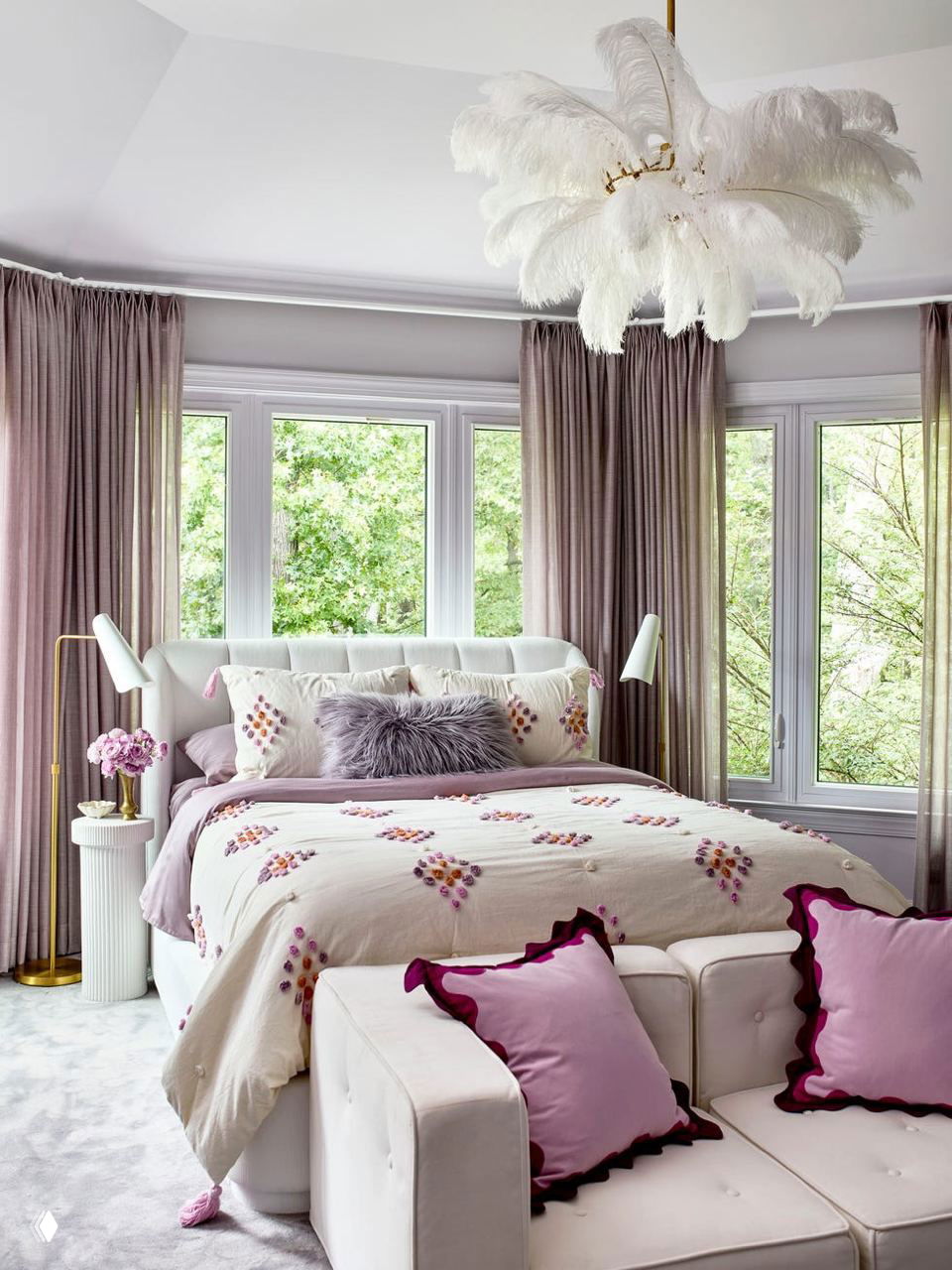 Спальня с округлой планировкой, мягкой кроватью и перьеобразной люстрой, пастельные текстильные акценты, диван и декоративные подушки у большого полукруглого окна.