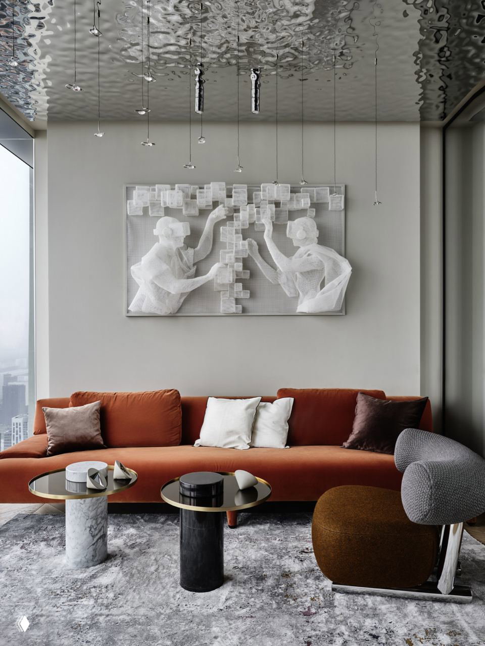 Современная гостиная с длинным оранжевым диваном на фоне серой декоративной панели и металлических столиков, интерьер с продуманной материальной фактурой