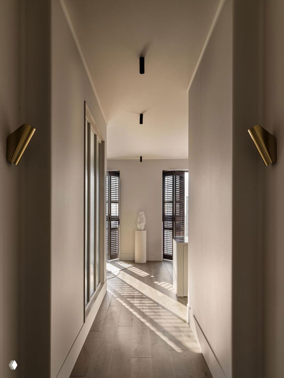 Длинный коридор с деревянным полом и колонной-стеллажом; направленные световые полосы создают ритм и зонируют пространство между комнатами.