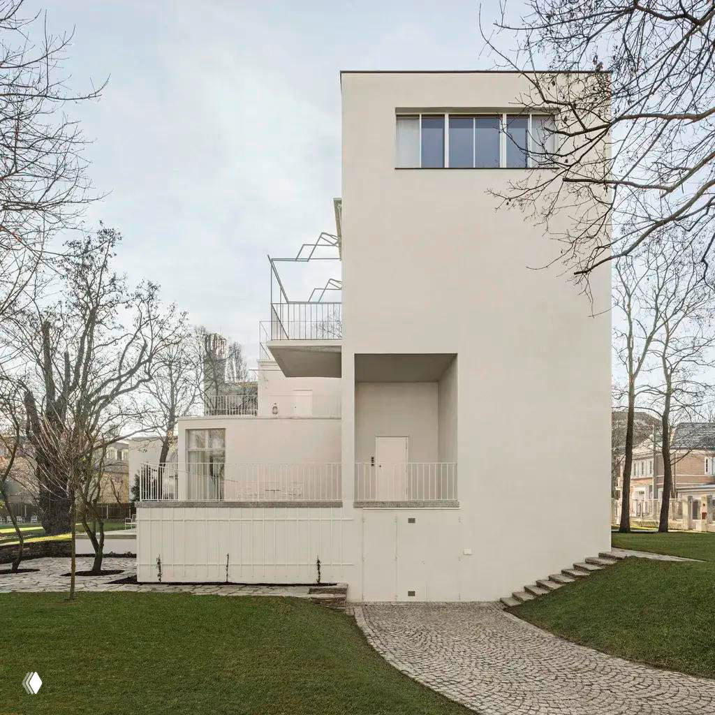 Боковой фасад виллы Beer с кубическими объёмами и террасами: чистые светлые формы, ступенчатая дорожка и газон вокруг памятника модернизма.