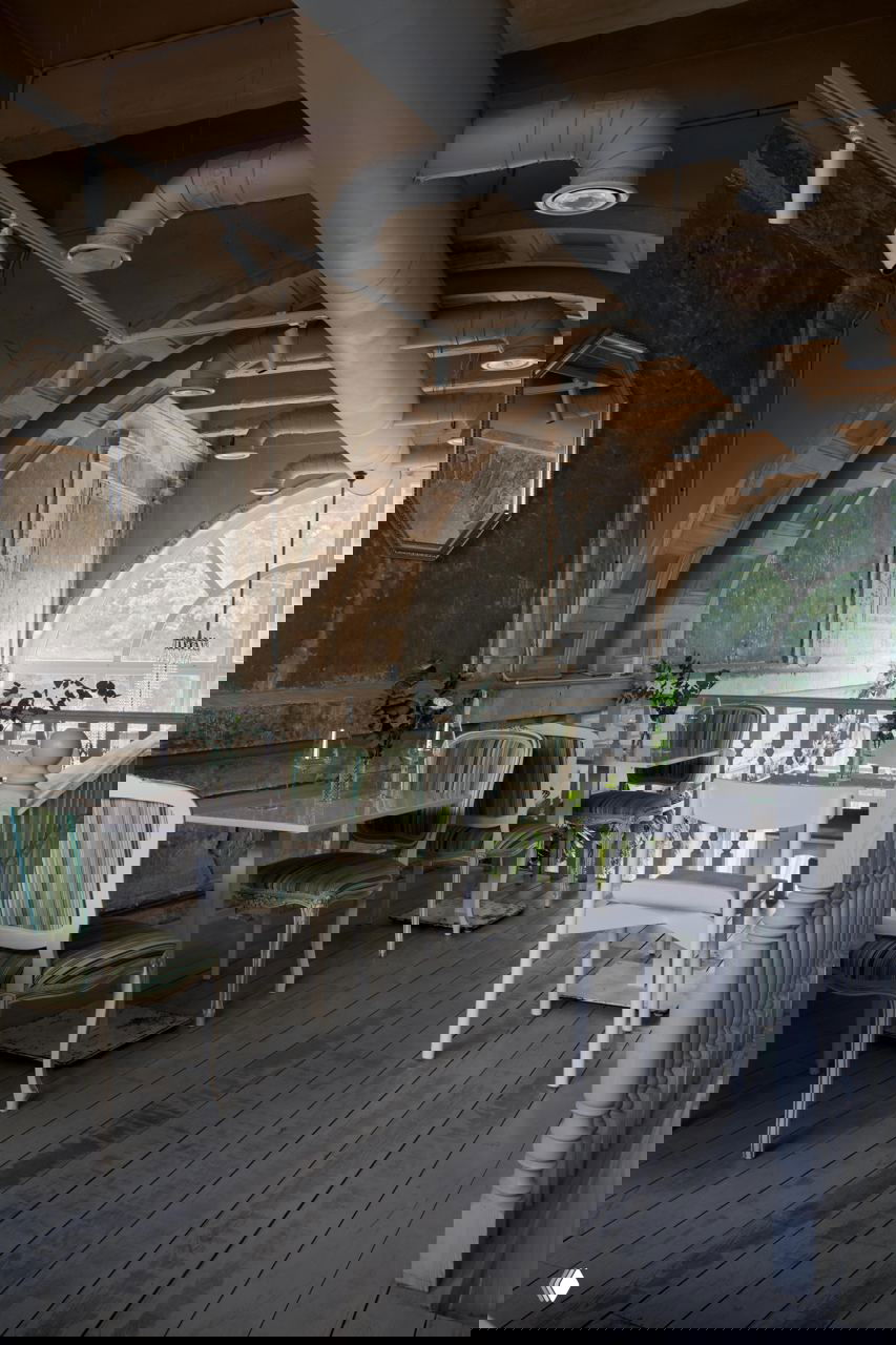 Арочная конструкция и потолочные вентиляционные трубы над галереей с полосатыми креслами и декоративными растениями на фоне старой фактуры стен.