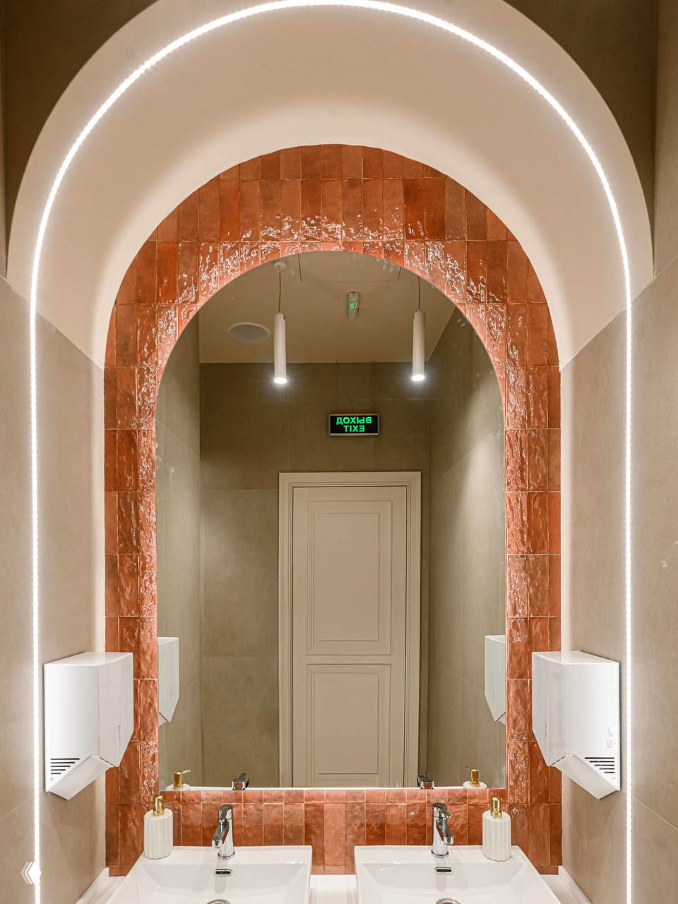 Санузел кафе с арочным проёмом, облицованным насыщенно-розово-терракотовой плиткой и встроенной светодиодной подсветкой по периметру.