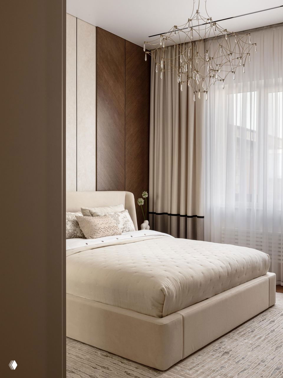 Спальня в нейтральных тёплых оттенках: мягкая кровать с текстильной обивкой, высокие шторы и декоративная стеновая панель из дерева и бежевого материала.