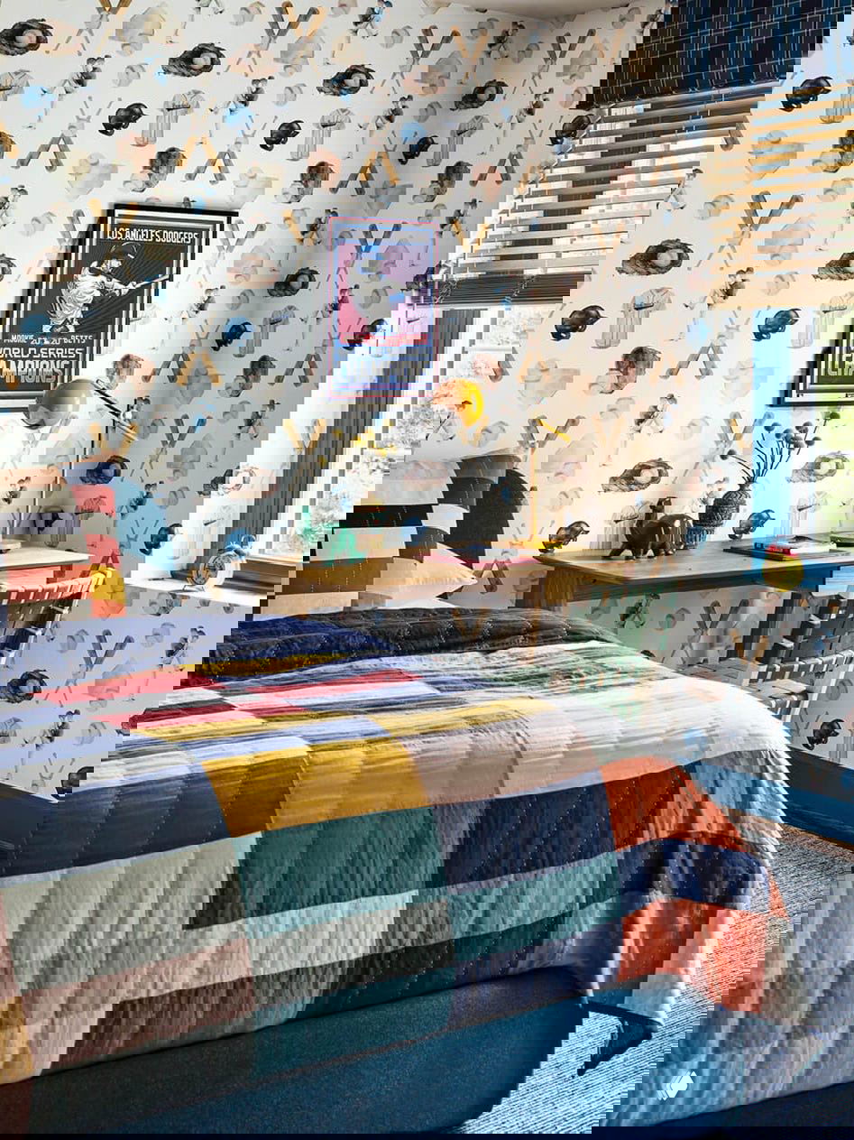 Детская спальня с тематическими обоями в бейсбольной стилистике, ярким лоскутным покрывалом на кровати, рабочим столом у окна и продуманными цветовыми акцентами для ребёнка.