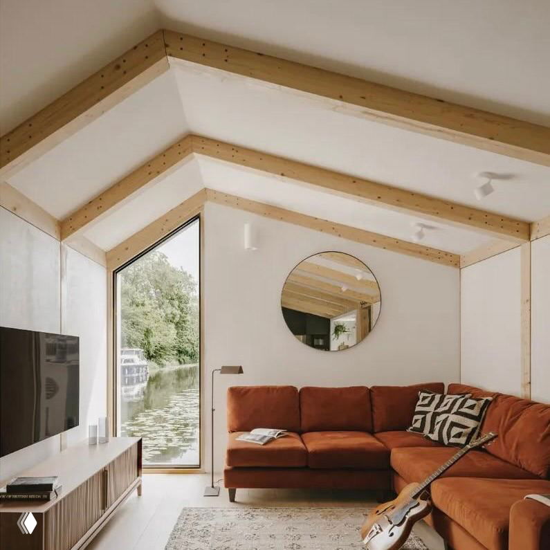 Гостиная с низким диваном и мансардной формой потолка: тёплая мягкая зона, окно с видом на канал и акустично оформленное пространство
