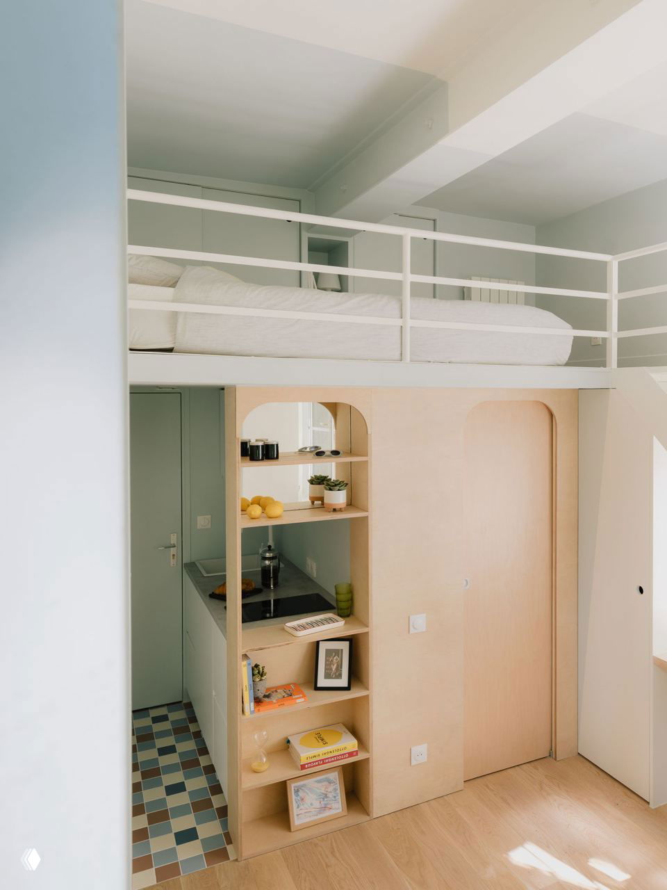 Мезонин с белыми перилами над мини-кухней и встроенными полками из светлой фанеры, организующими хранение и подчеркивающими морскую эстетику проекта.