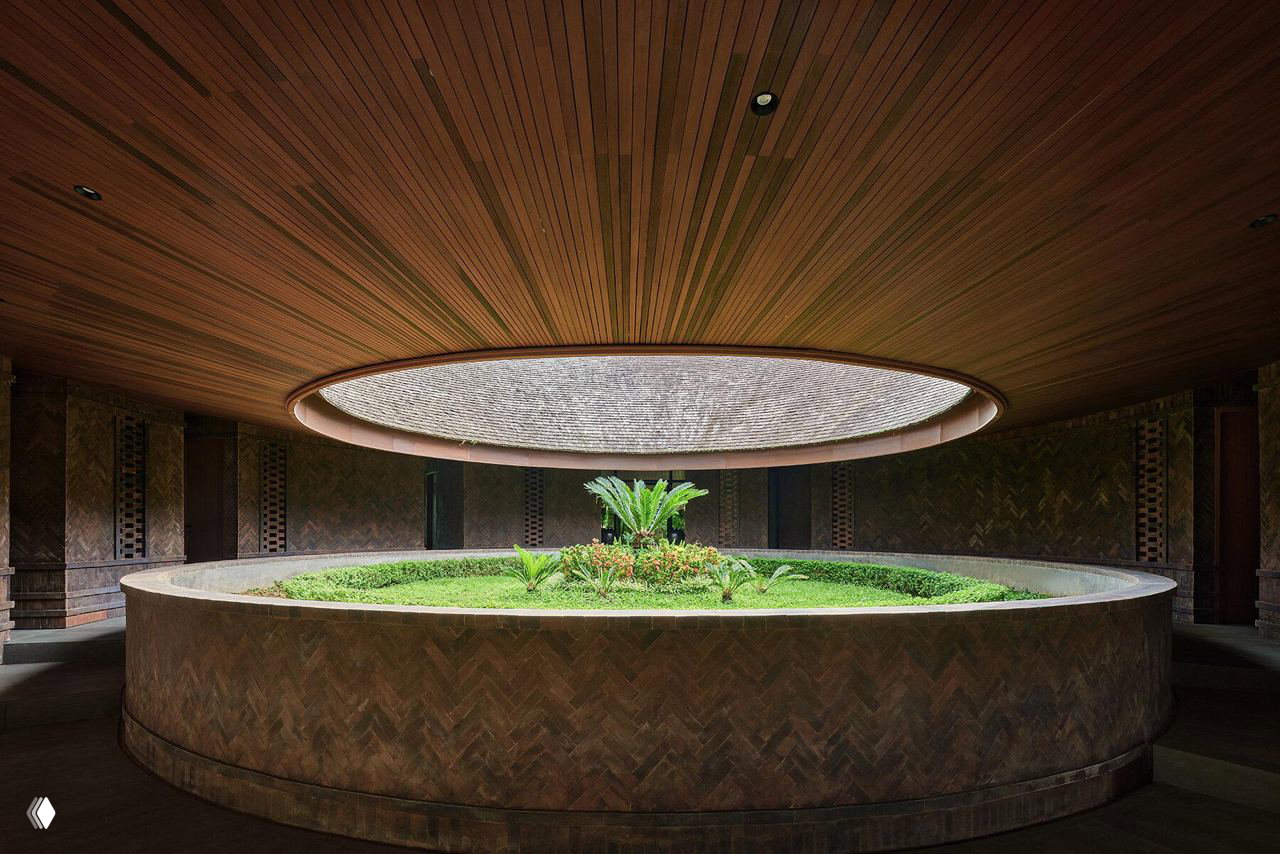 Вид внутреннего двора виллы: круглое садовое пространство с низкой стеной и центральным зелёным ядром под овальным световым отверстием в крыше.