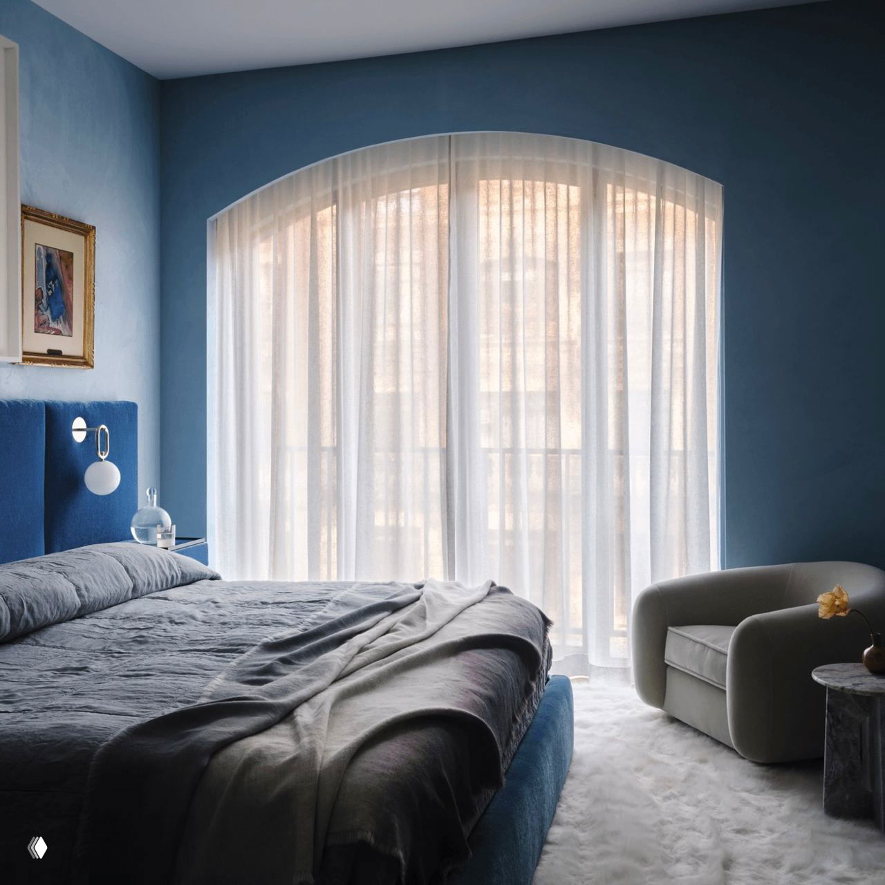 Главная спальня в спокойных синих тонах: синий мягкий изголовье, белый пушистый ковёр и большие занавеси, создающие умиротворяющий фон для картин.