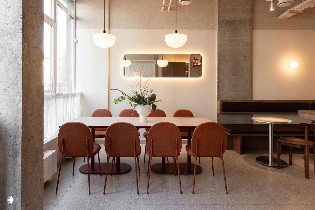 Столовая зона бистро Buno: большой белый стол и шесть терракотовых стульев, зеркало и декоративные светильники создают уютную композицию.