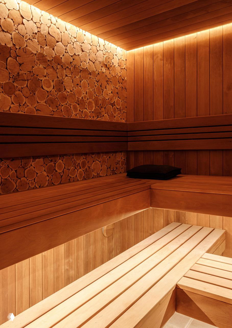 Сауна с деревянной обшивкой, лавками и декоративной стеной из поперечных спилов дерева, подсвеченная тёплым боковым светом для уюта.