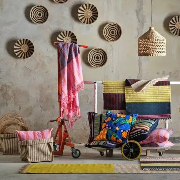 Сцена с ковриками, подушками и текстилем в зелёно‑жёлтой и розовой палитре; на потолке виден плетёный светильник, акцент — тканые принты.