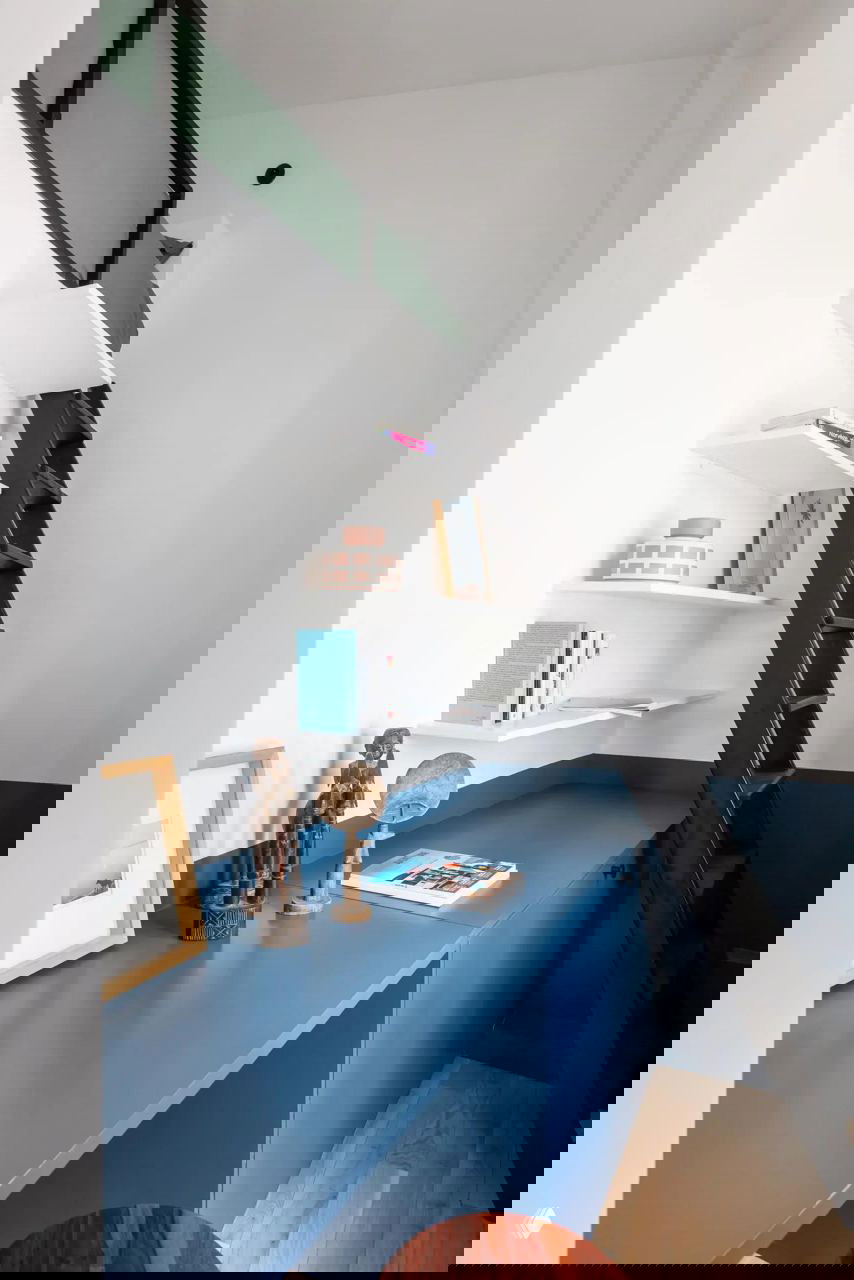 Рабочее место и антресоль: встроенная синяя столешница и шкафы, узкая лестница на антресоль и минималистичный декор в компактном парижском пространстве.