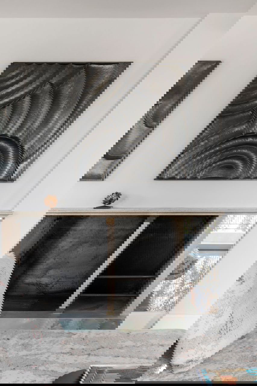 Деталь интерьера с металлическими рельефными панно над камином и низким стеллажом, выдержанная в нейтральной гамме с акцентами современного искусства.