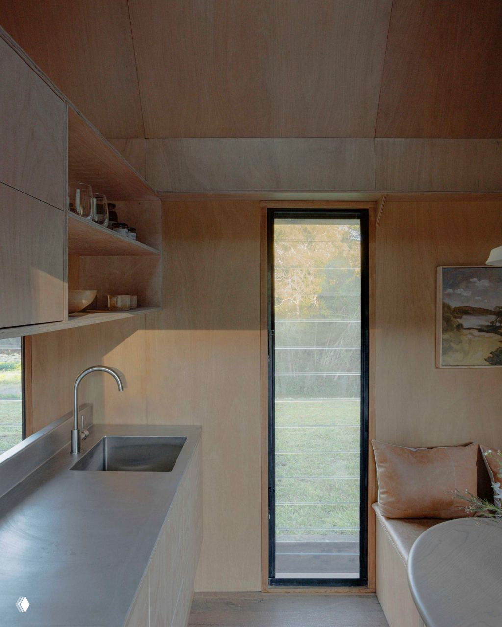 Мини‑кухня внутри The Oculus: моечная секция из металла, простая столешница и открытые полки на фоне светлой фанеры.