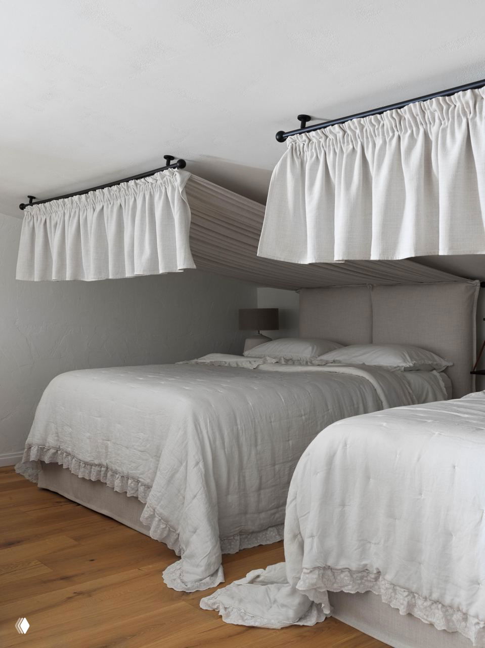 Две кровати под парящими белыми потолочными балдахинами в мансардном пространстве, натуральный лен и спокойная светлая палитра текстиля.