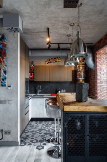 Кухонная зона с барной стойкой и индустриальными светильниками, металлические поверхности и кирпичная кладка в интерьере.