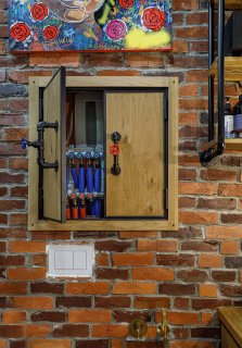Деталь интерьера: деревянный настенный шкафчик с коллекцией ключей и предметов на фоне красной кирпичной кладки и рабочих деталей.