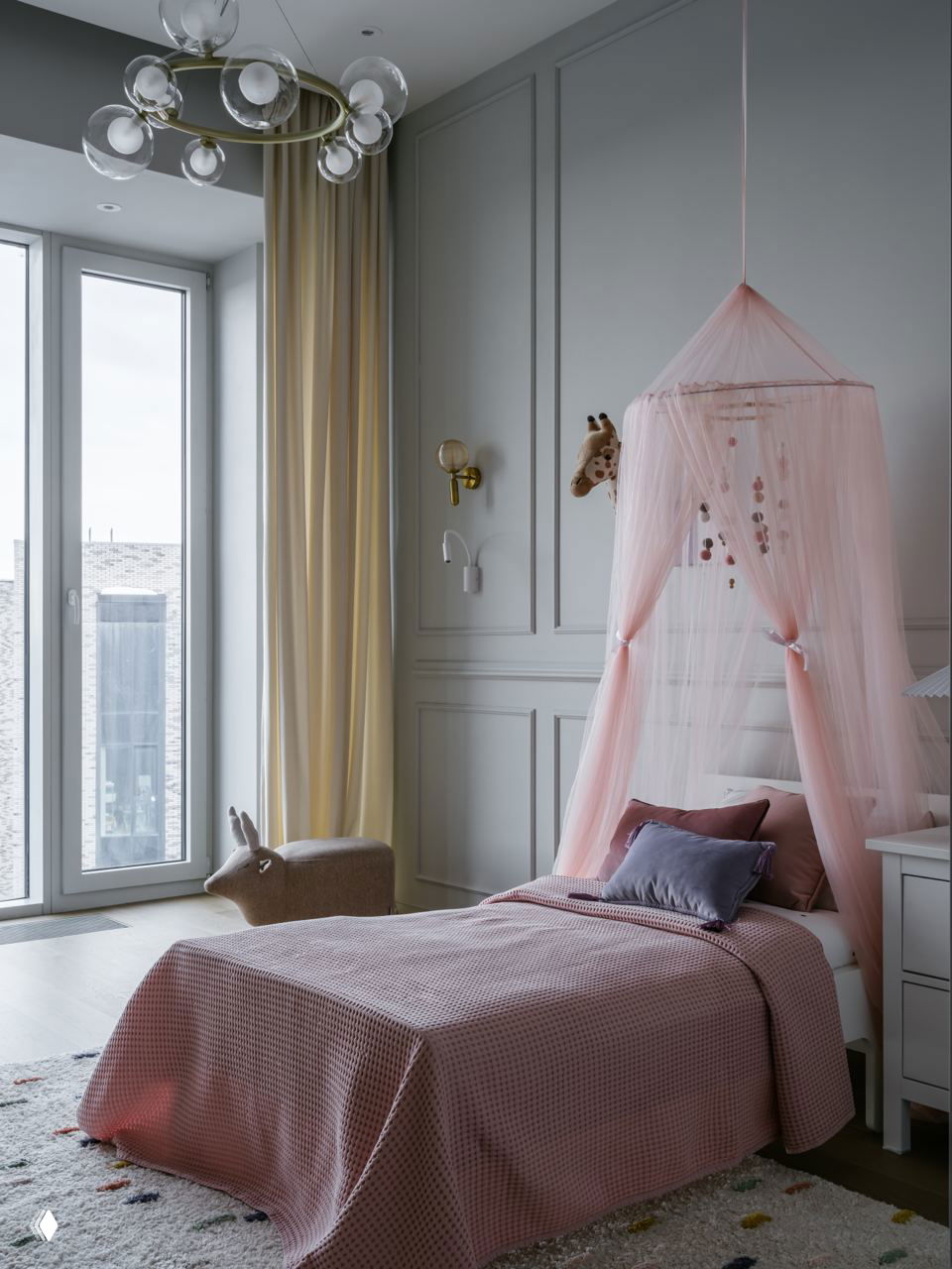 Высокое окно и нежно-розовый круглый балдахин над односпальной кроватью, светлый интерьер с классическими панелями и пастельным текстилем.