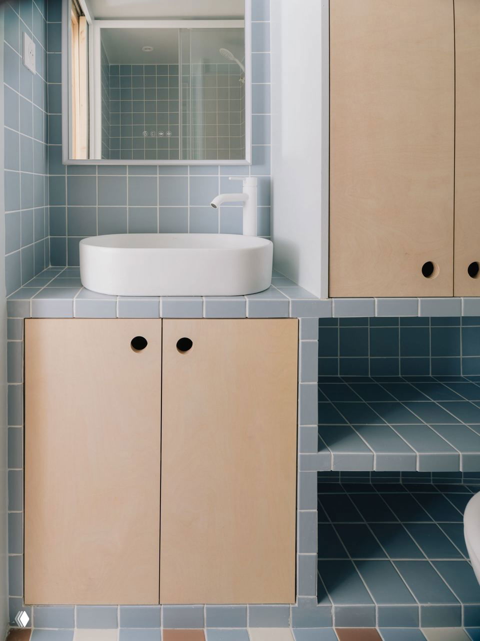 Светлый уголок под лестницей с рабочим столом и табуретом, большая оконная ниша и деревянные ступени, формирующие уютный дневной угол в студии.