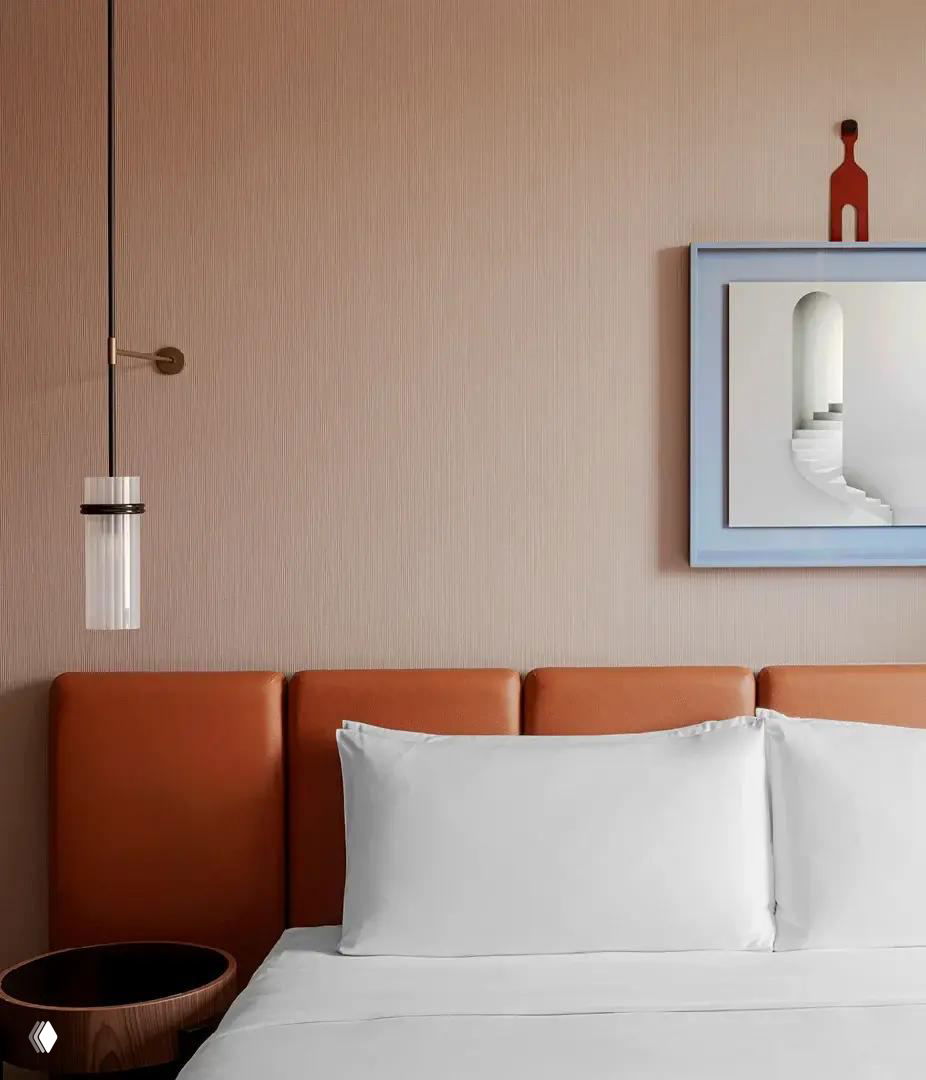 Кровать в номере Casa Brera: кожаное изголовье терракотового оттенка, белое постельное белье и декоративная картина на пастельной стене.