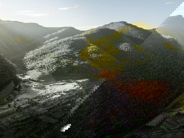 Панорамный вид на театр, встроенный в долину между покрытыми лесом и бамбуком холмами, подчёркивающий масштаб и связь с ландшафтом.