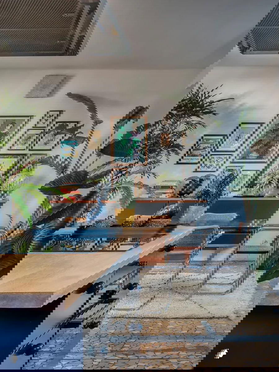 Кухонная зона с островом и деревянной столешницей, декоративной коллекцией картин на стене, зелёными растениями и мозаичным напольным покрытием.