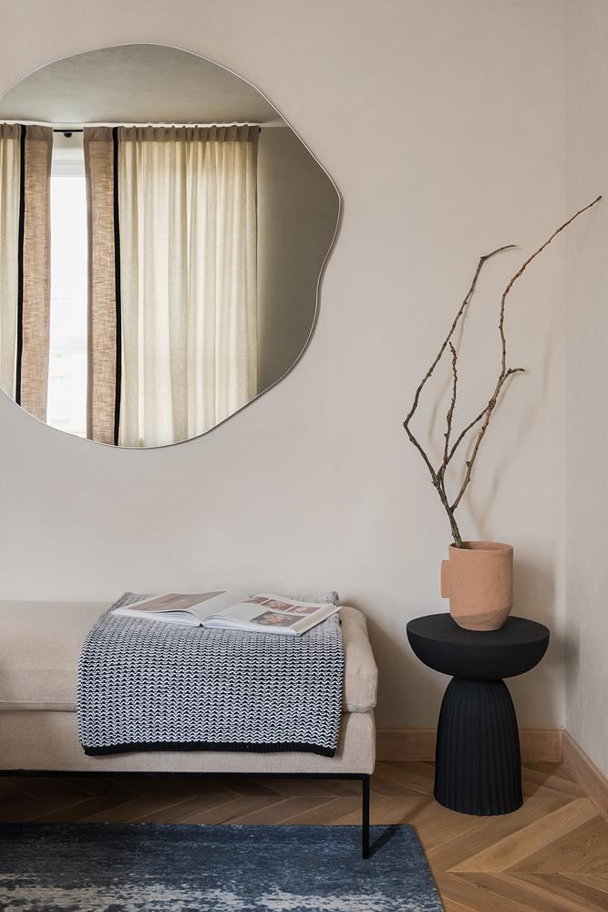 Прихожая или зона ожидания с асимметричным круглым зеркалом, скамьёй и минималистскими декоративными акцентами; светлая, спокойная палитра и текстуры.