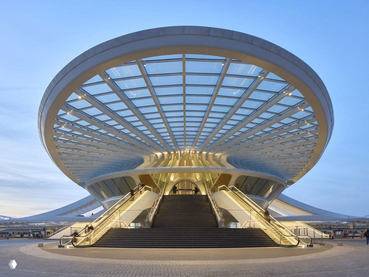 Входная группа под круглой навесной конструкцией вокзала в Монсе: лестницы, эскалаторы и стеклянная крыша с конструктивными ребрами.