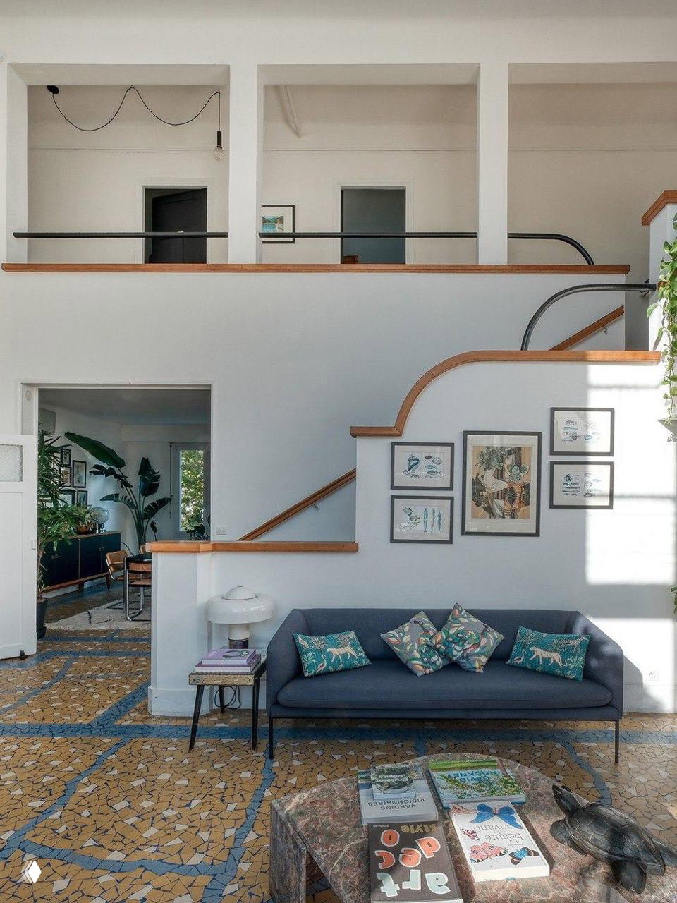 Гостиная и лестничная зона с мезонином, диваном у стены, рельефными перилами и продолжением мозаичного пола под ступенями.