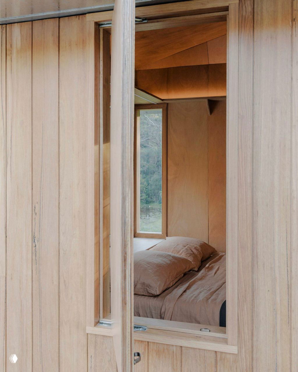 Вид в спальню через дверной проём: деревянные панели, минималистичная кровать и вертикальное окно для естественного света.