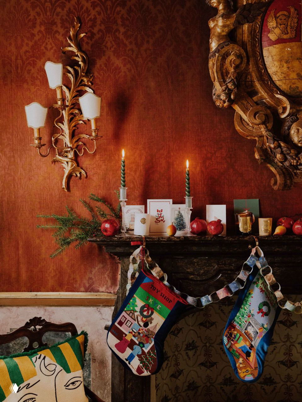 Деталь камина с праздничными чулками, бумажной гирляндой, зажжёнными свечами и новогодними открытками на бархатной стене палаццо.