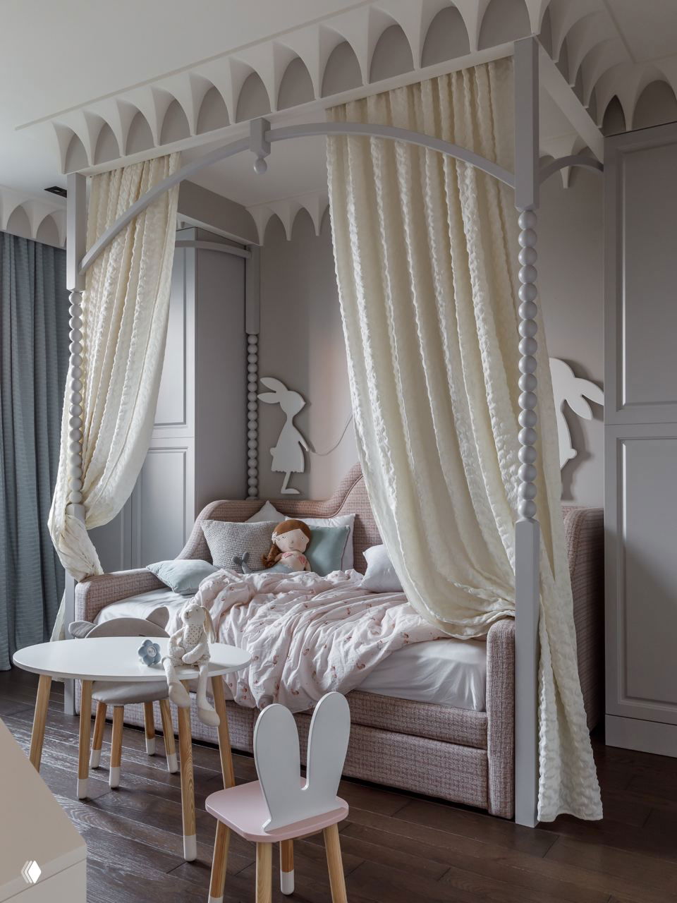 Романтичная детская с балдахином на каркасе: кремовые плотные шторы, мягкий диван-кровать, игрушки и столик для творчества на деревянном полу.
