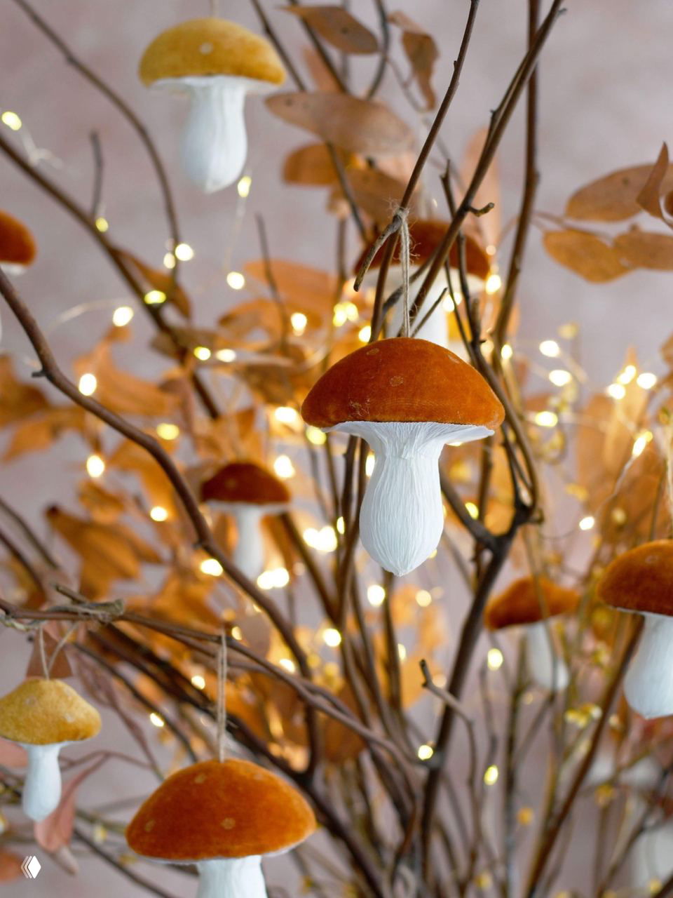 Ветви с подвесными бархатными грибами и тёплой гирляндой — нежная осенняя инсталляция, подходящая для хэллоуинских «ёлок» и интерьерных композиций.