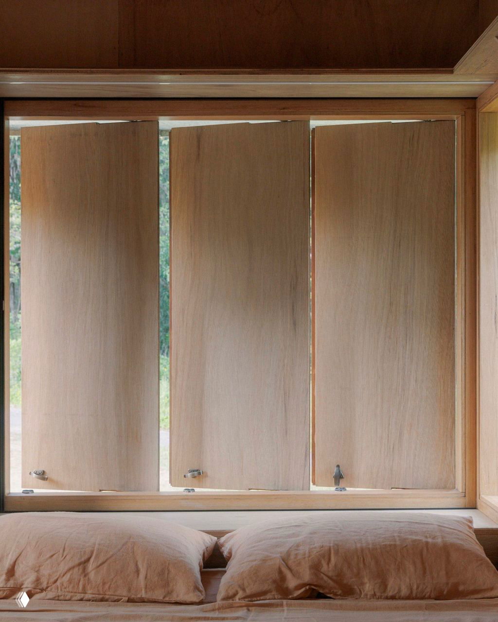 Раздвижные деревянные ставни и кровать у окна: текстура фанеры, натуральная палитра и продуманный контроль света в интерьере.