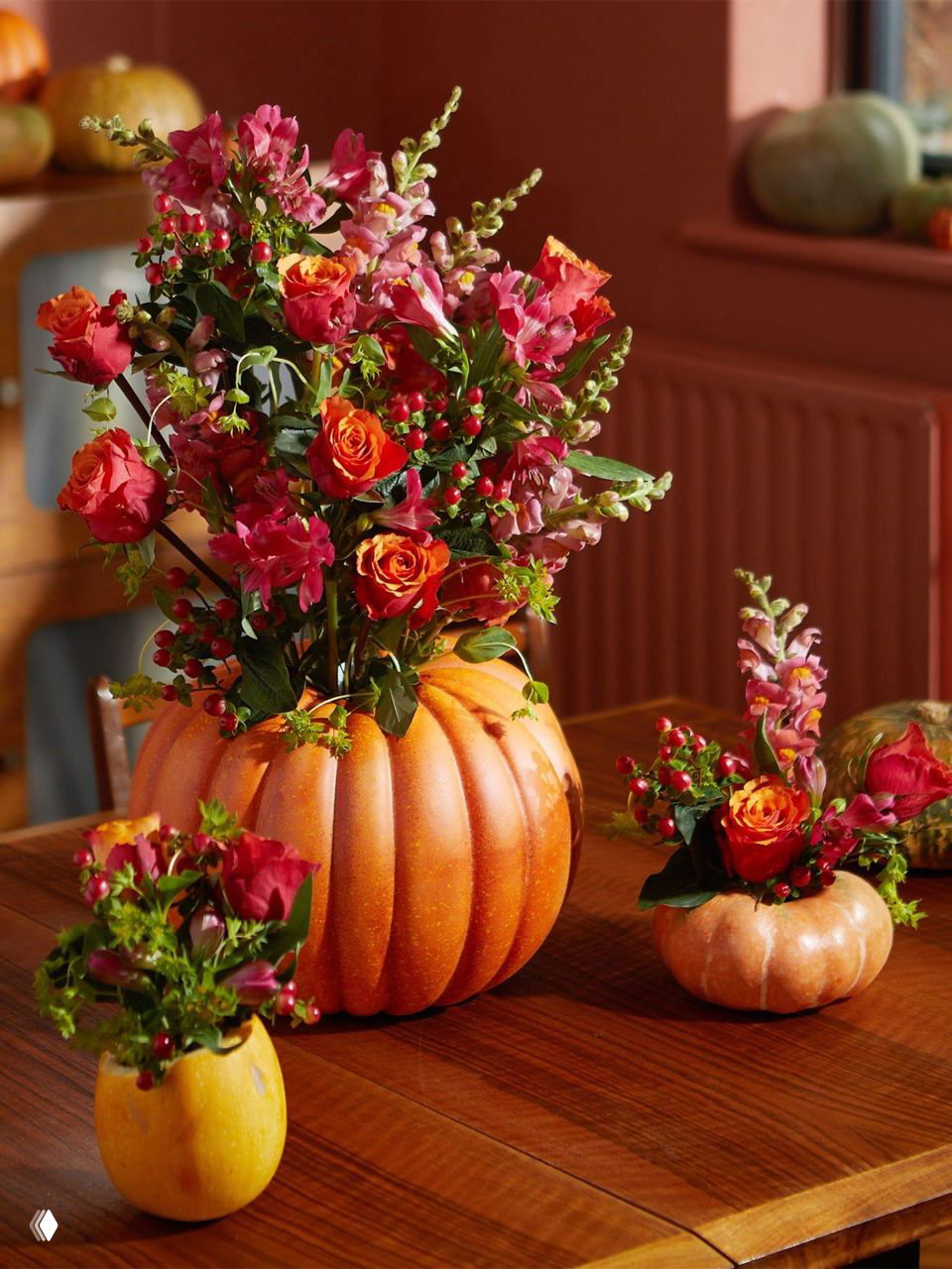 Вазы, вырезанные из тыкв и наполненные букетами: крупная и несколько маленьких на деревянном столе как тёплый гостеприимный центр композиции.