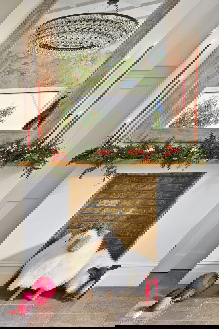 Каминная зона с зеркалом и гирляндой из хвои, на полу пушистые фигурки овец — сочетание традиционных и причудливых рождественских элементов.