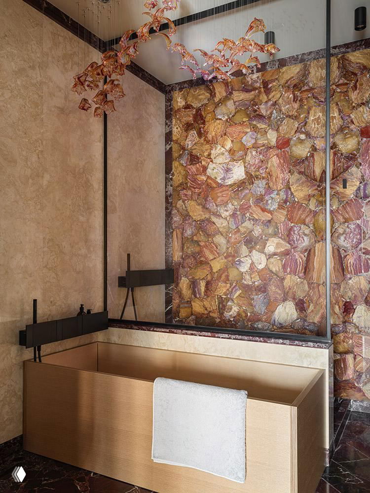 Ванная комната с панно из разноцветного натурального камня за ванной и минималистичной прямоугольной ванной, сочетающейся с темными каменными полами.