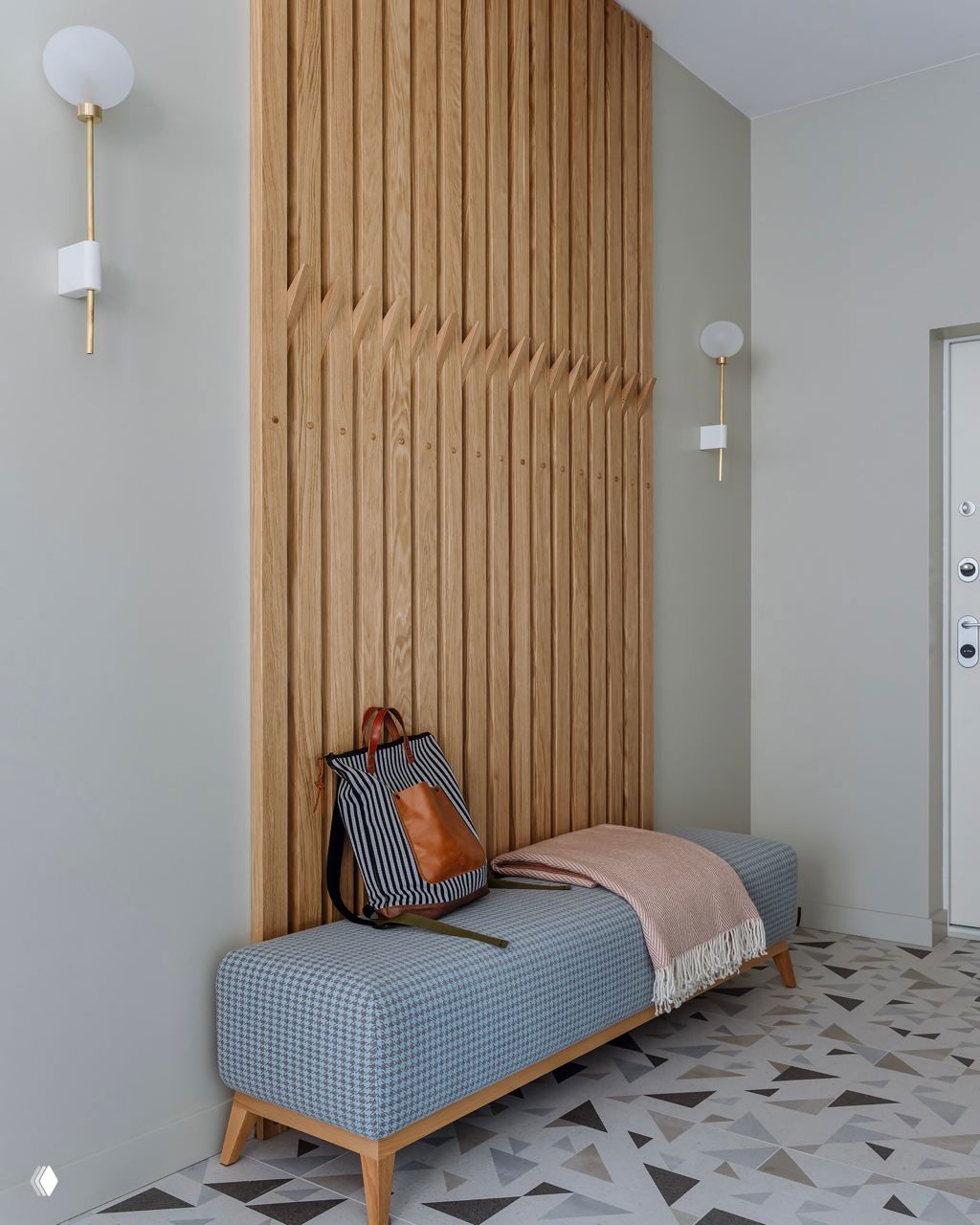 Прихожая с вертикальной деревянной панелью и длинной скамьёй; на полу светлые плитки с абстрактным геометрическим узором в спокойных тонах.