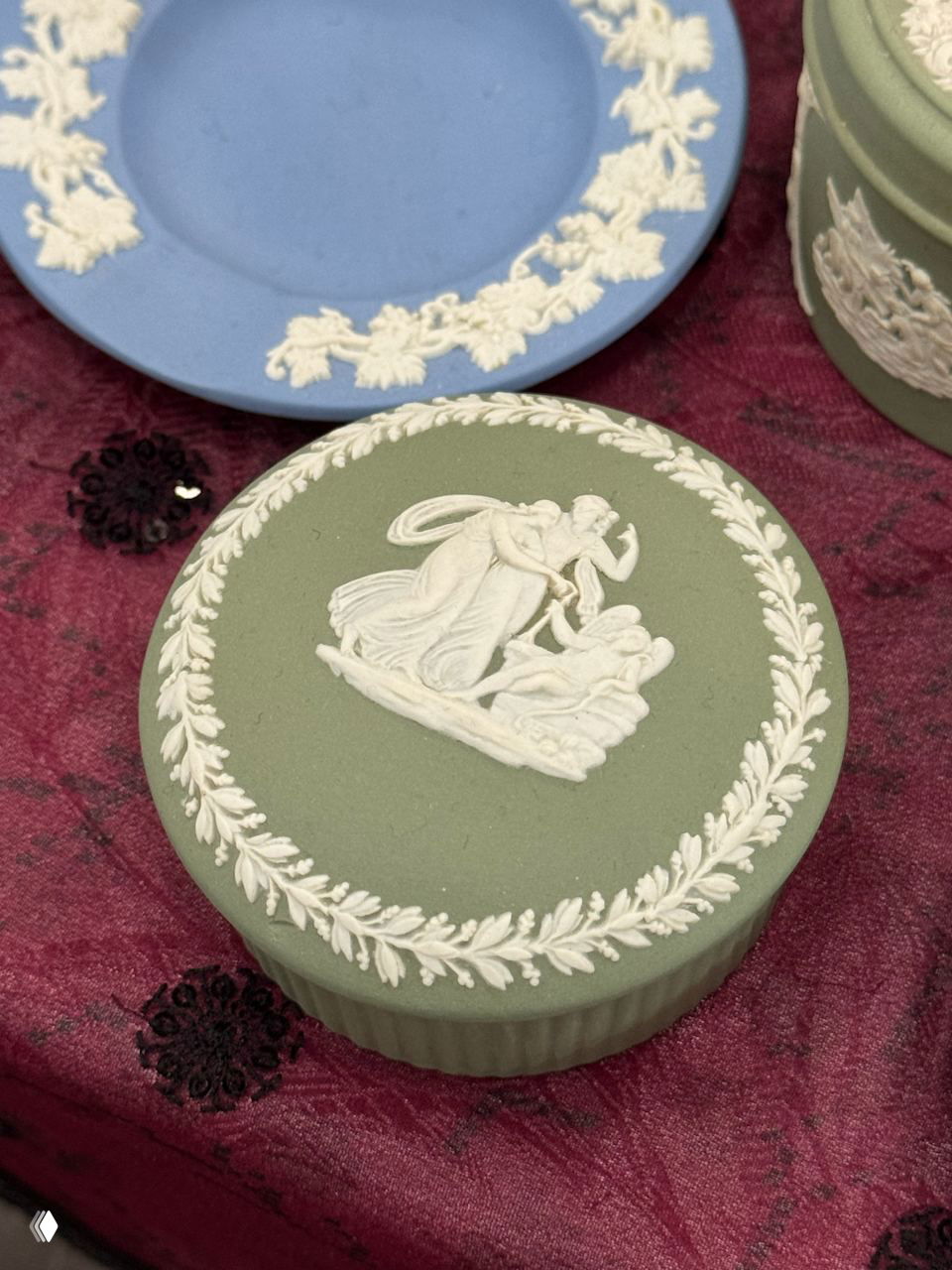 Круглая шкатулка в стиле Wedgwood светло-зелёного цвета с классическим белым рельефным орнаментом, выставленная на столе маркета.