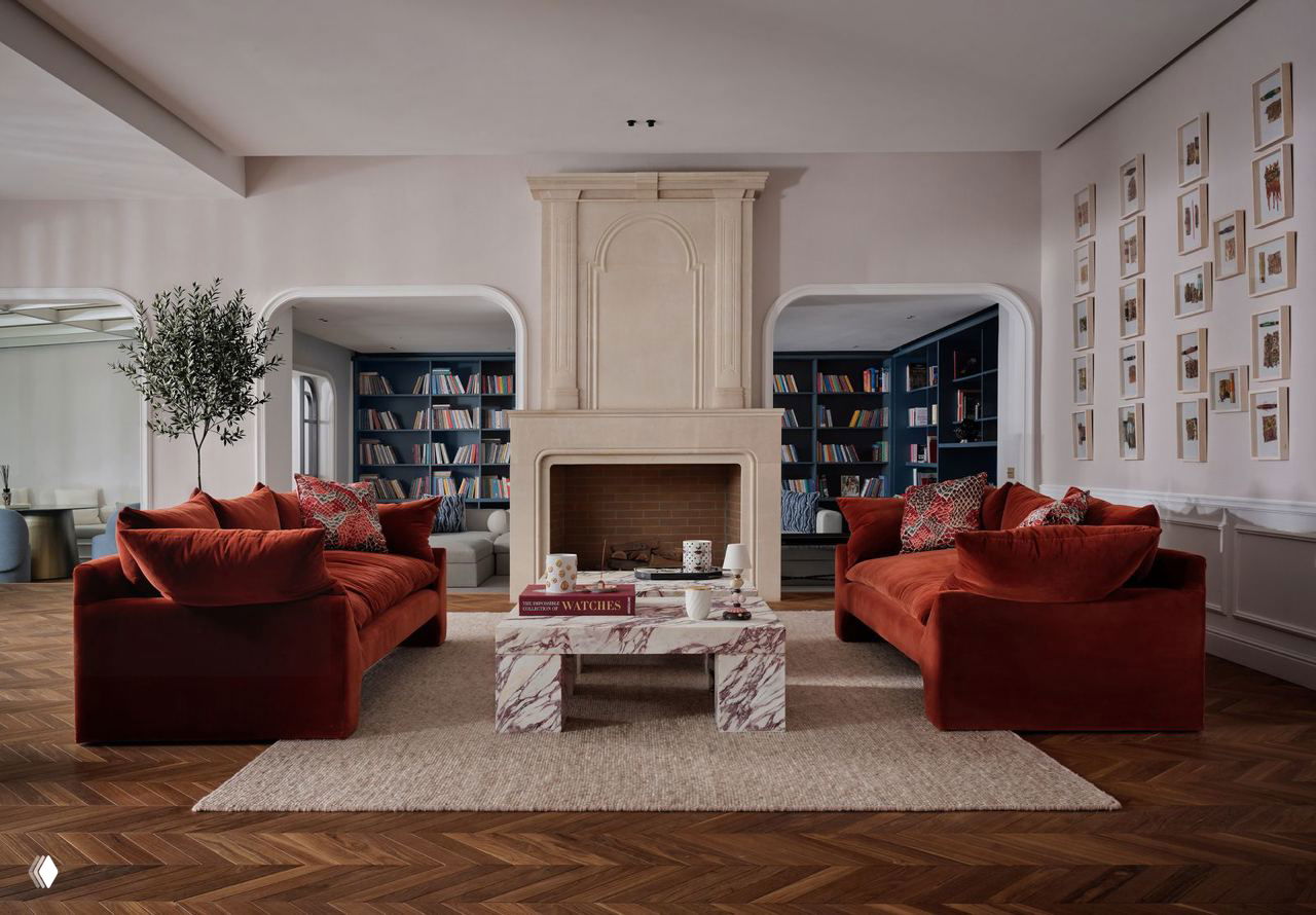 Симметричная гостиная с двумя бархатными красными диванами напротив камина и мраморным столом — тёплая палитра.