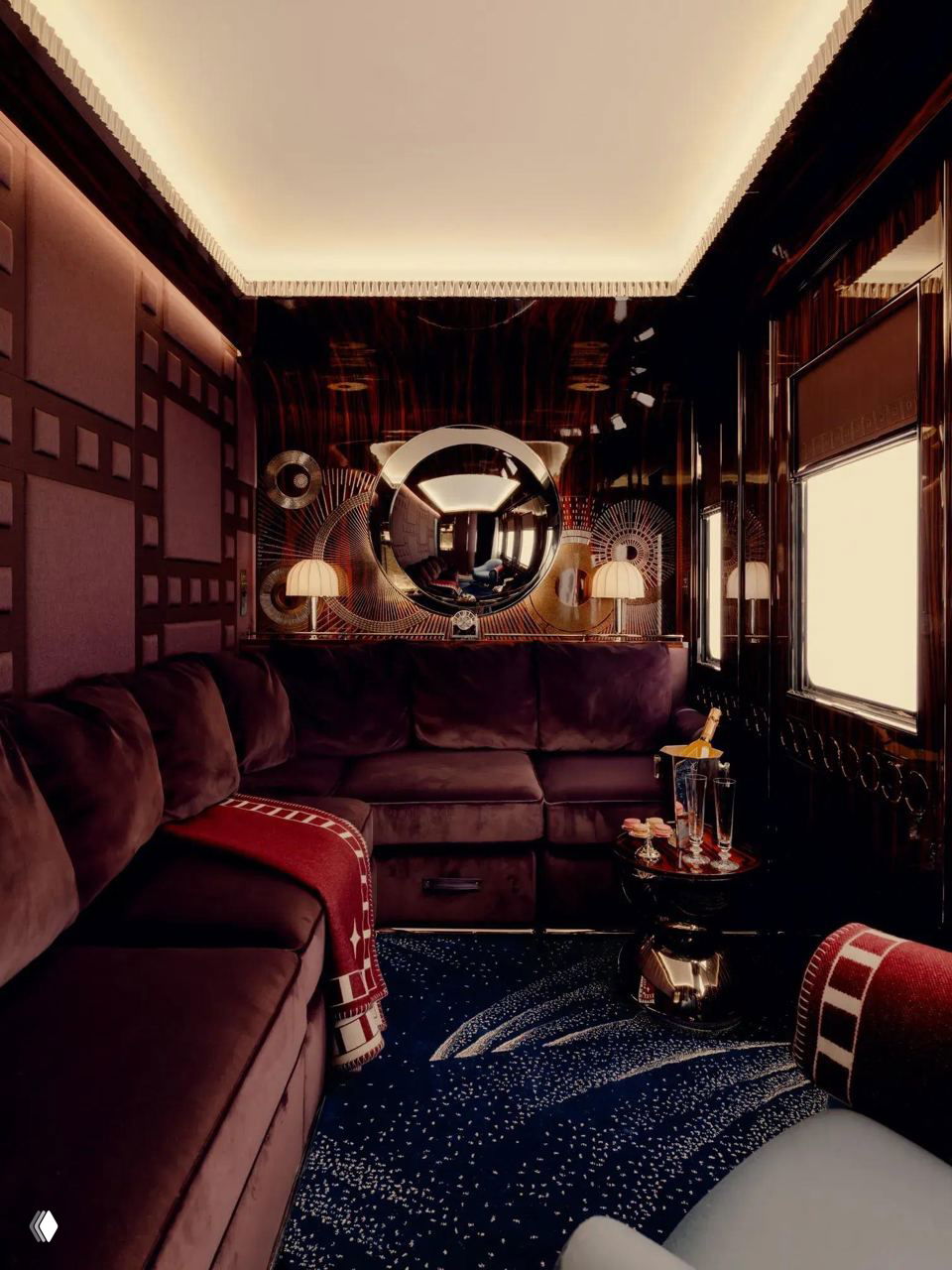 Салон вагона с диваном тёмно‑бордового цвета, круглым зеркалом и сложной декоративной панелью — сочетание зеркал, стекла Lalique и резных элементов.