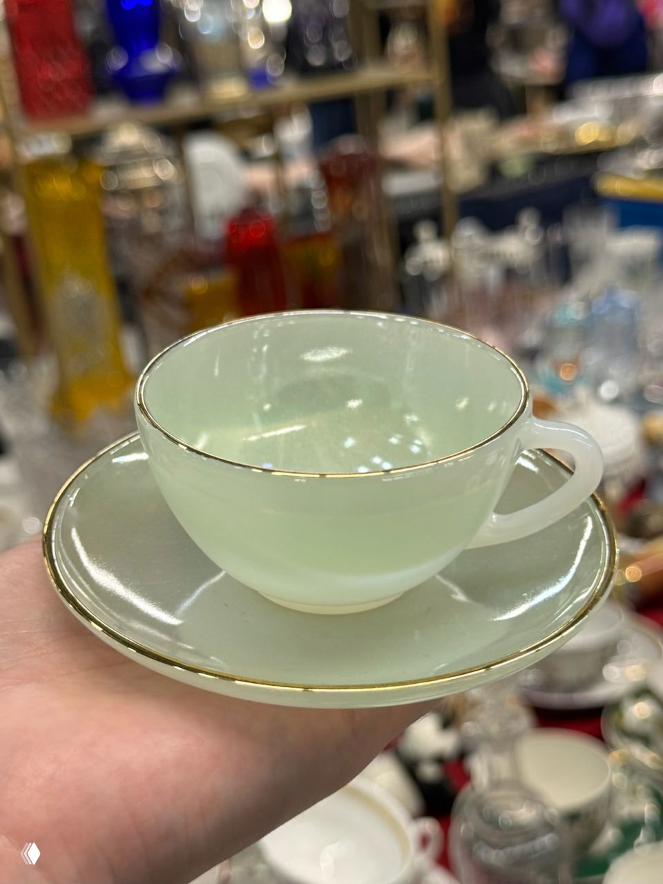 Светлая фарфоровая чашка с блюдцем с тонким золотым ободком, поднесённая на ладони для показа покупателям на маркете.