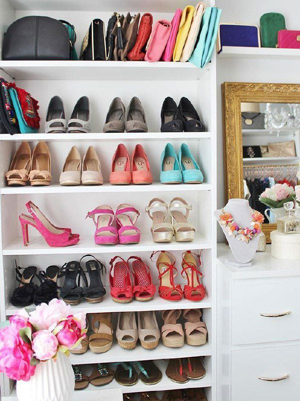 Открытый белый шкаф с множеством полок, аккуратно организованные туфли разных цветов и сумки на верхних полках в ярком интерьере.