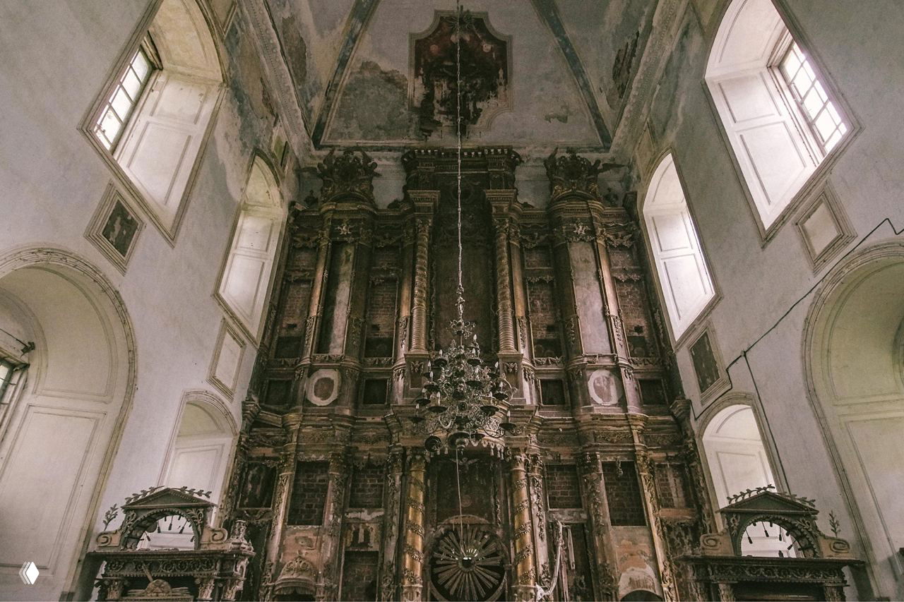 Интерьер церкви с высоким старинным иконостасом и алтарной частью; видны следы времени, потемнения и повреждения на отделке и иконах.