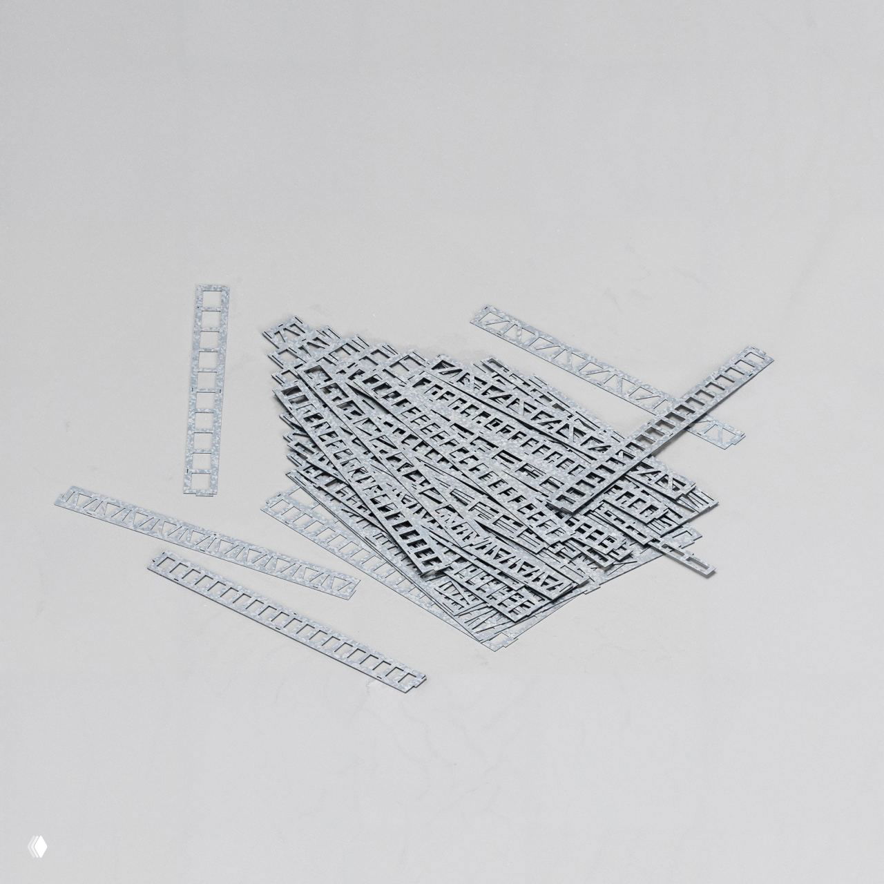 Набор отдельных деталей стального конструктора: вырезанные полосы и элементы из оцинкованной стали толщиной 0,6 мм, разложенные на светлом фоне